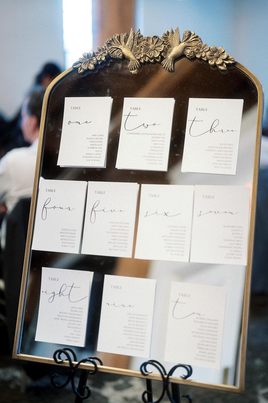 Wedding seating chart cards displayed on an ornate gold-framed mirror.