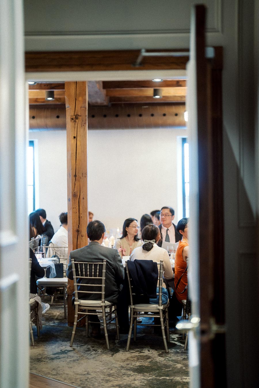 Guests seated at banquet tables inside a rustic event space viewed through a doorway