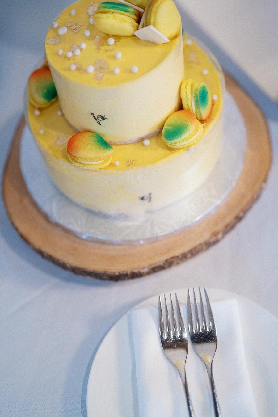Two-tier yellow cake with macarons beside a plate and forks