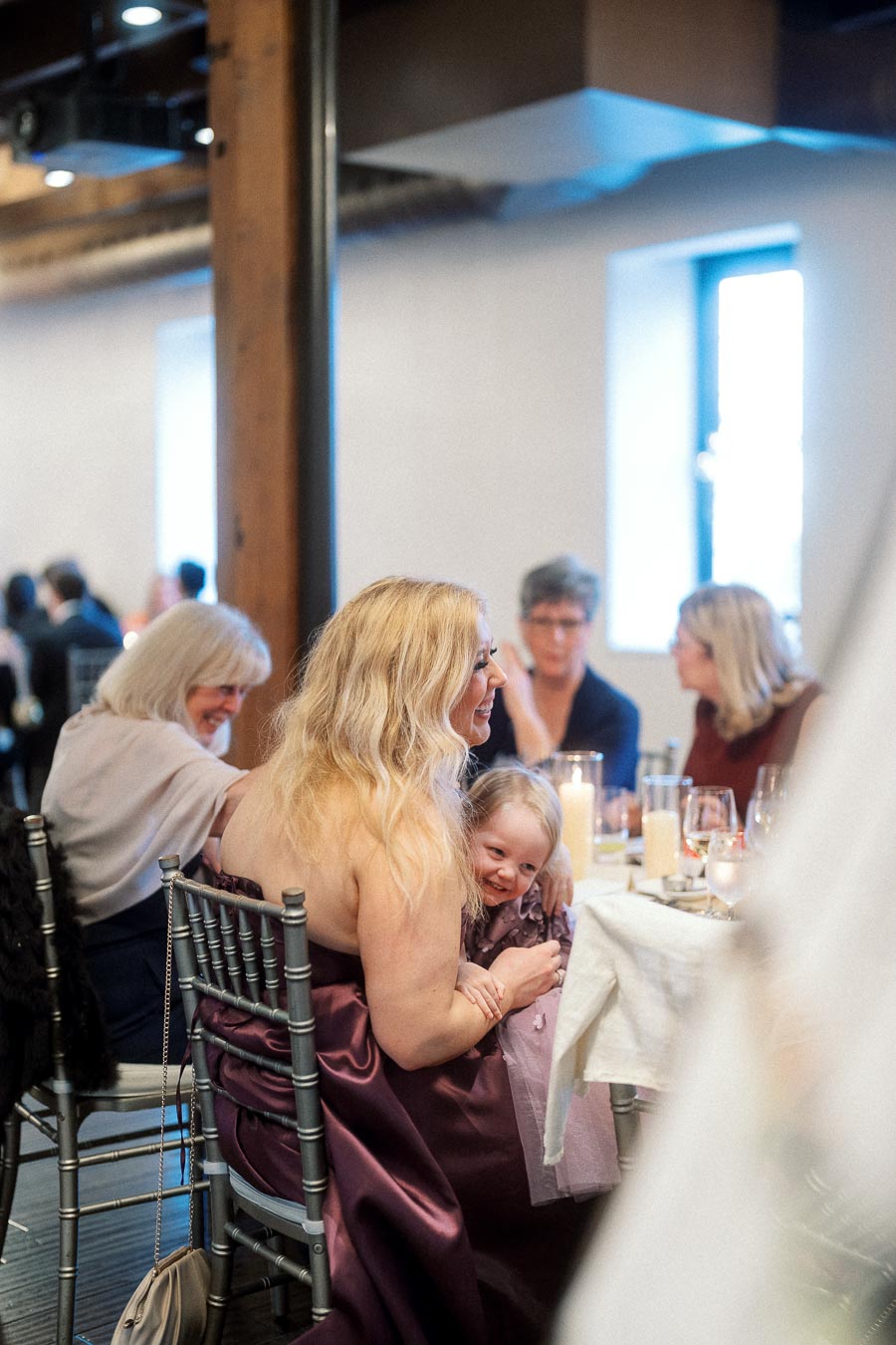 Woman in a burgundy dress holding a smiling child at a reception table.