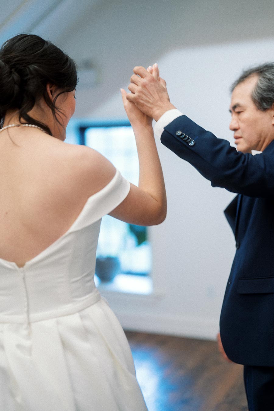 Woman in a white dress holds hands with a man in a navy suit indoors