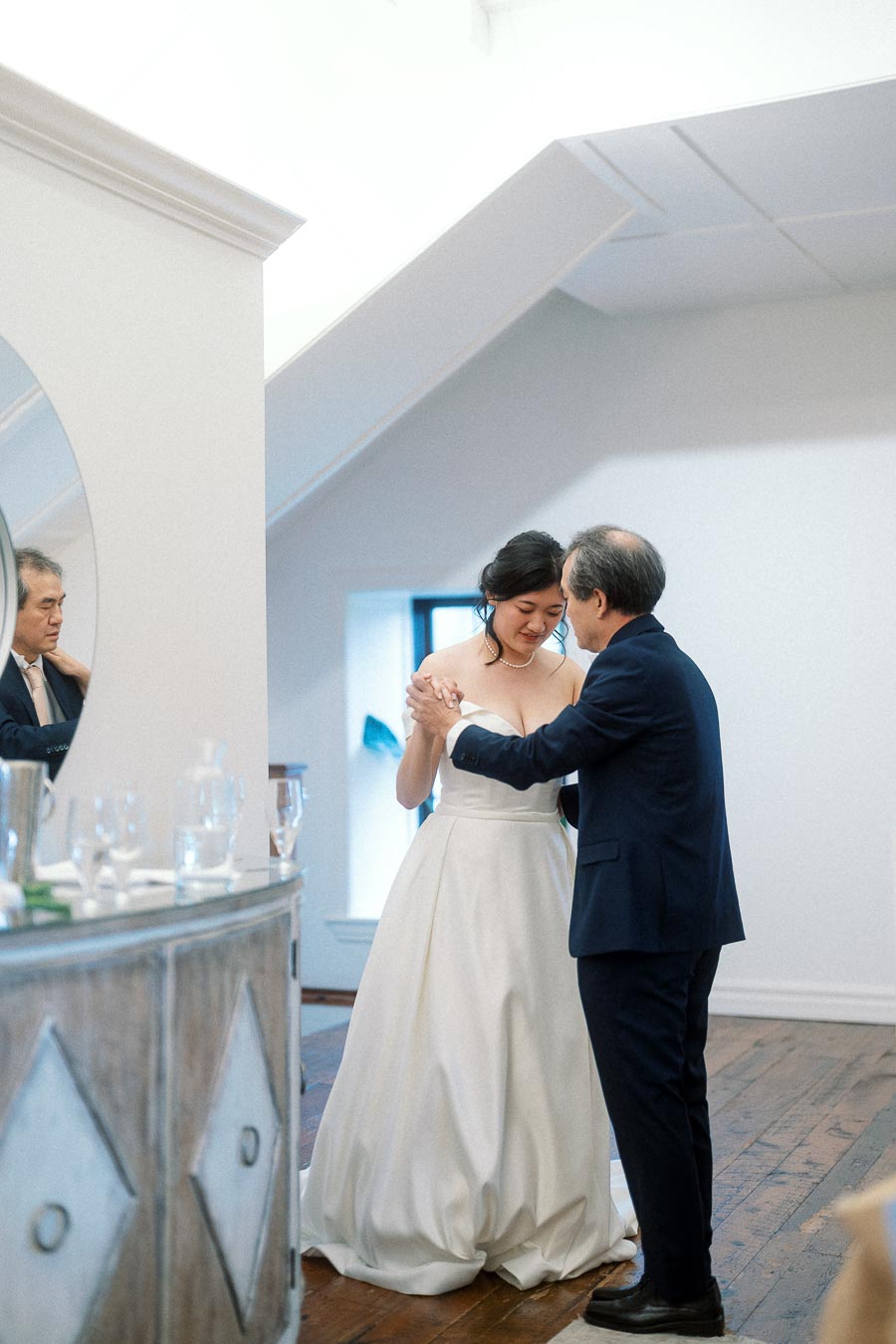 Woman in a white gown dancing with an older man in a bright indoor room