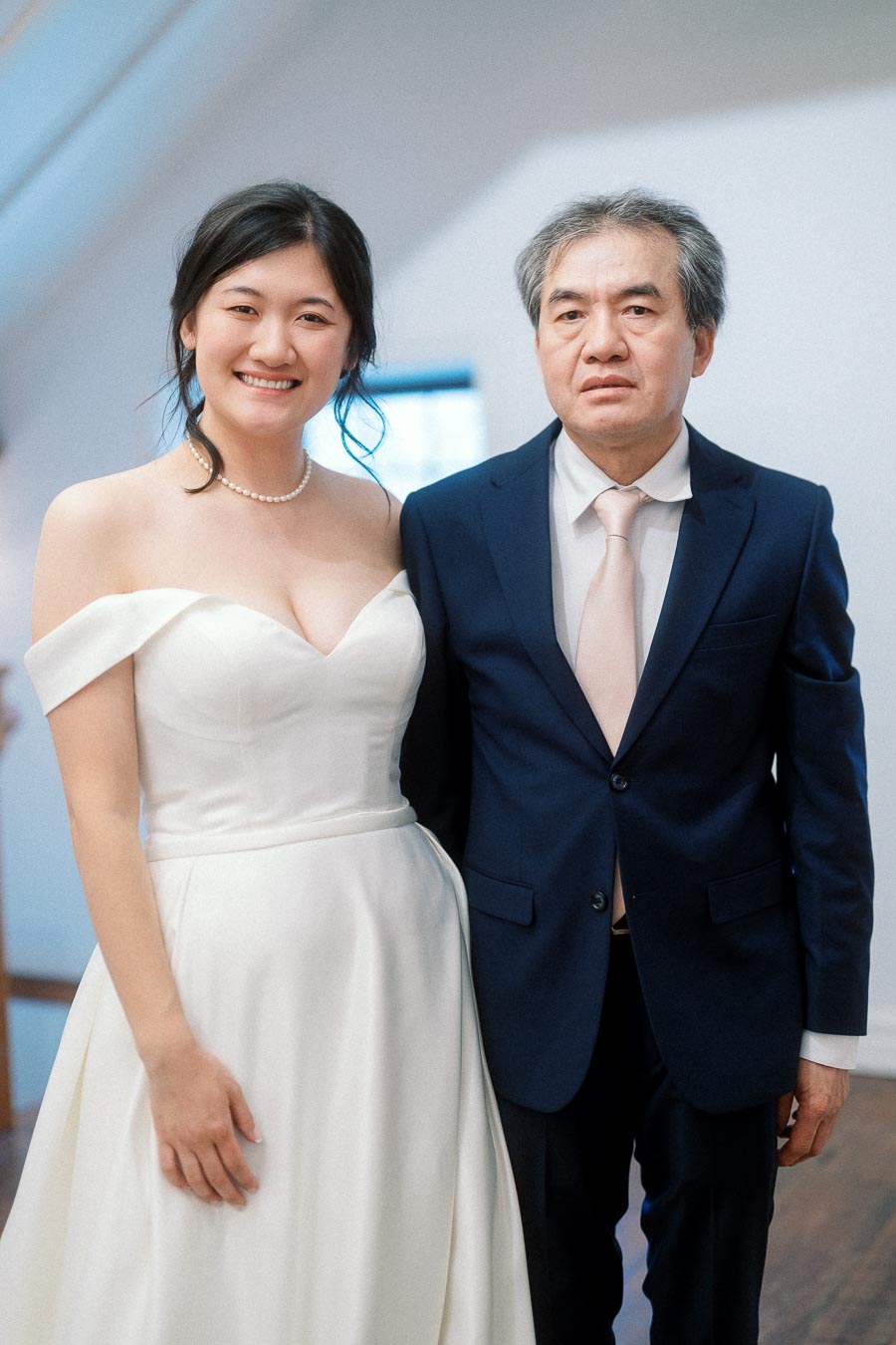 Woman in a white dress standing beside a man in a navy suit indoors