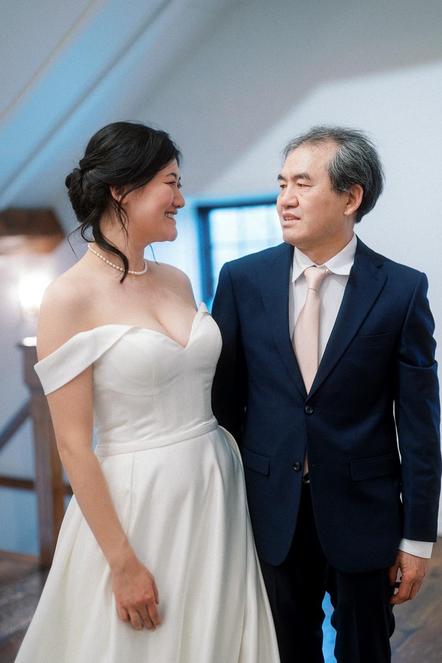 Woman in an off-the-shoulder white gown smiling at a man in a navy suit