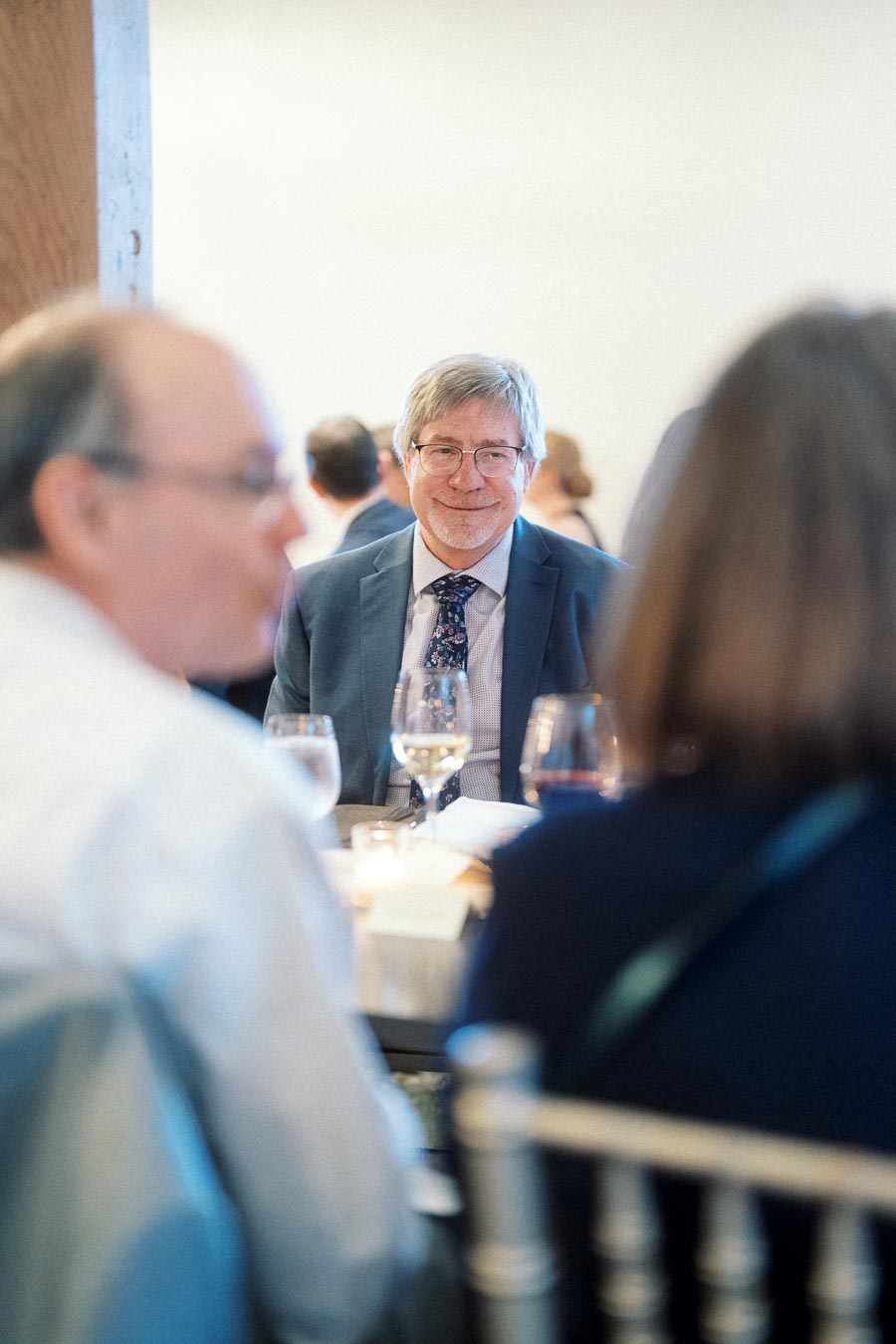 Man in a suit smiling across a table at a formal indoor dinner