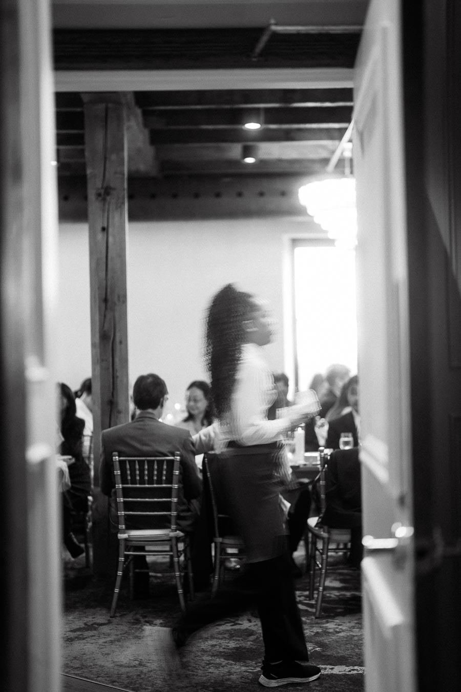 Black and white view through a doorway of guests seated at an indoor event.