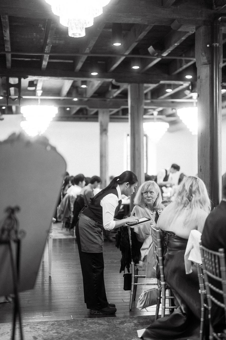 Server taking an order from a seated guest in a busy reception hall