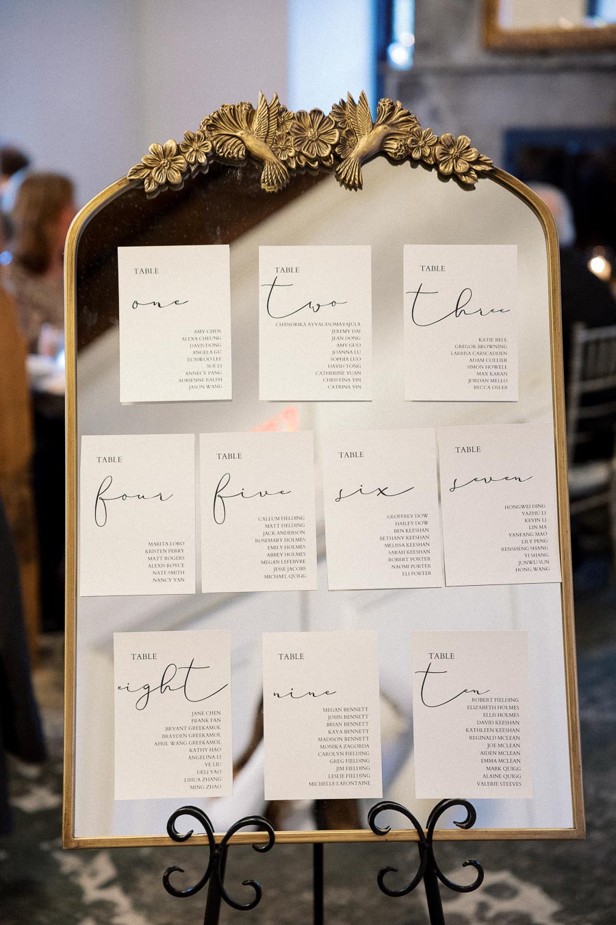 Gold-framed mirror displaying table assignment cards on a black easel.