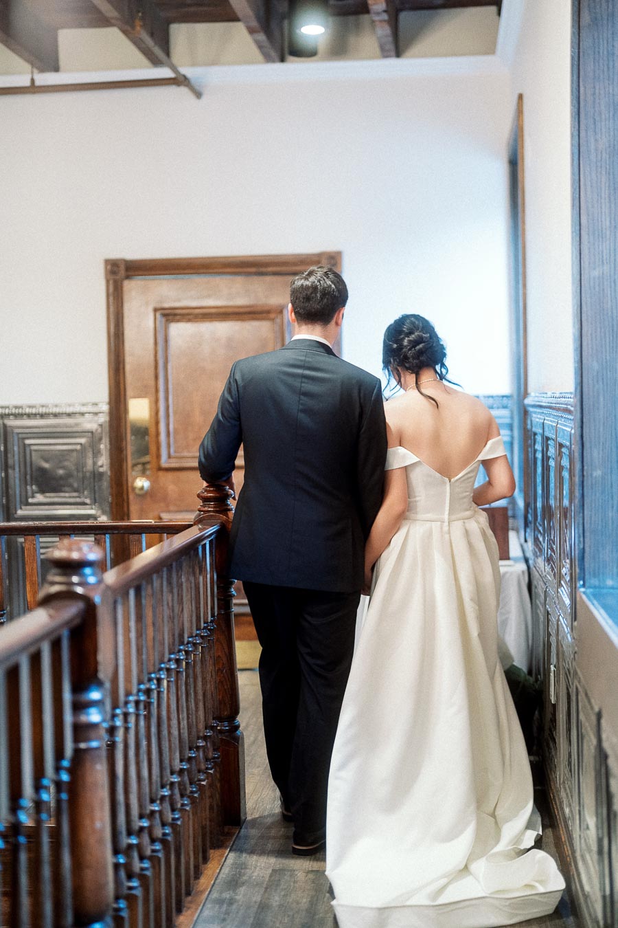 Couple in formal wedding attire walking down a wood-paneled interior hallway