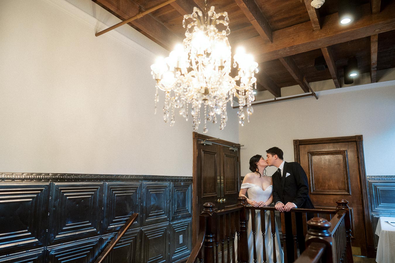 Couple kissing on an indoor staircase beneath a crystal chandelier.
