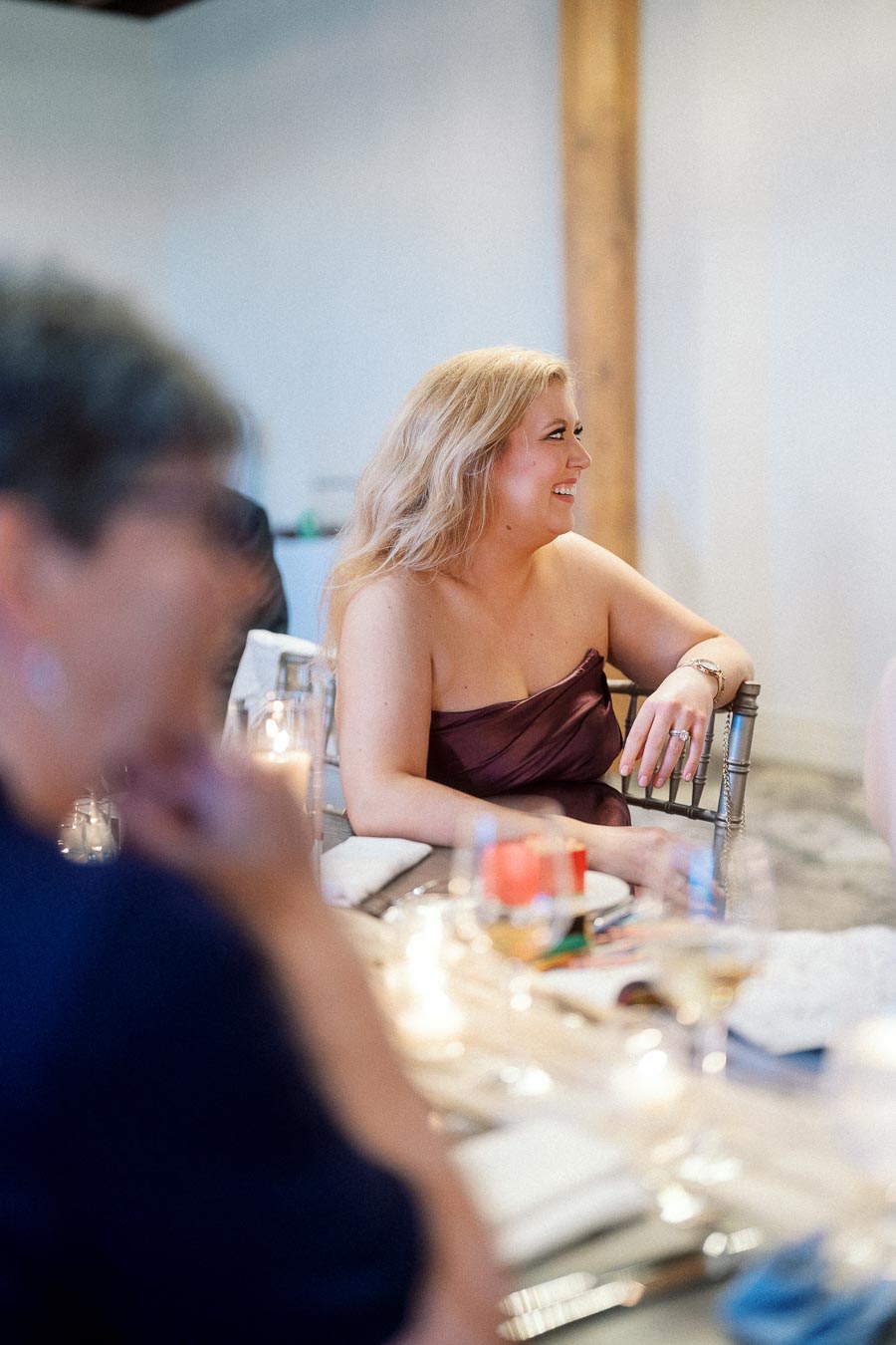 Woman in a burgundy dress laughing at a candlelit dinner table
