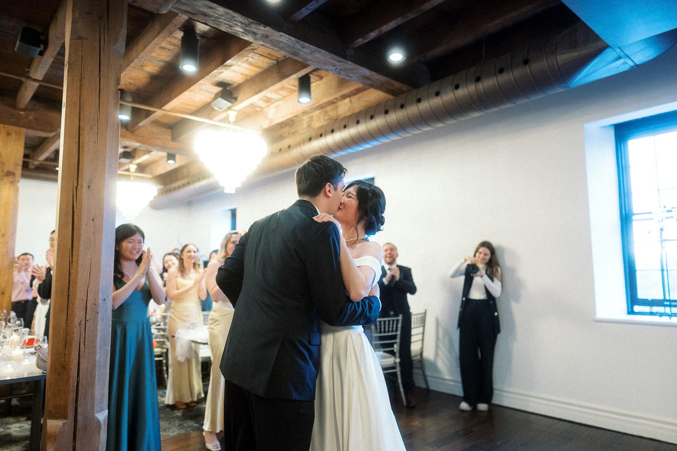 Couple kissing while guests applaud during an indoor engagement celebration.
