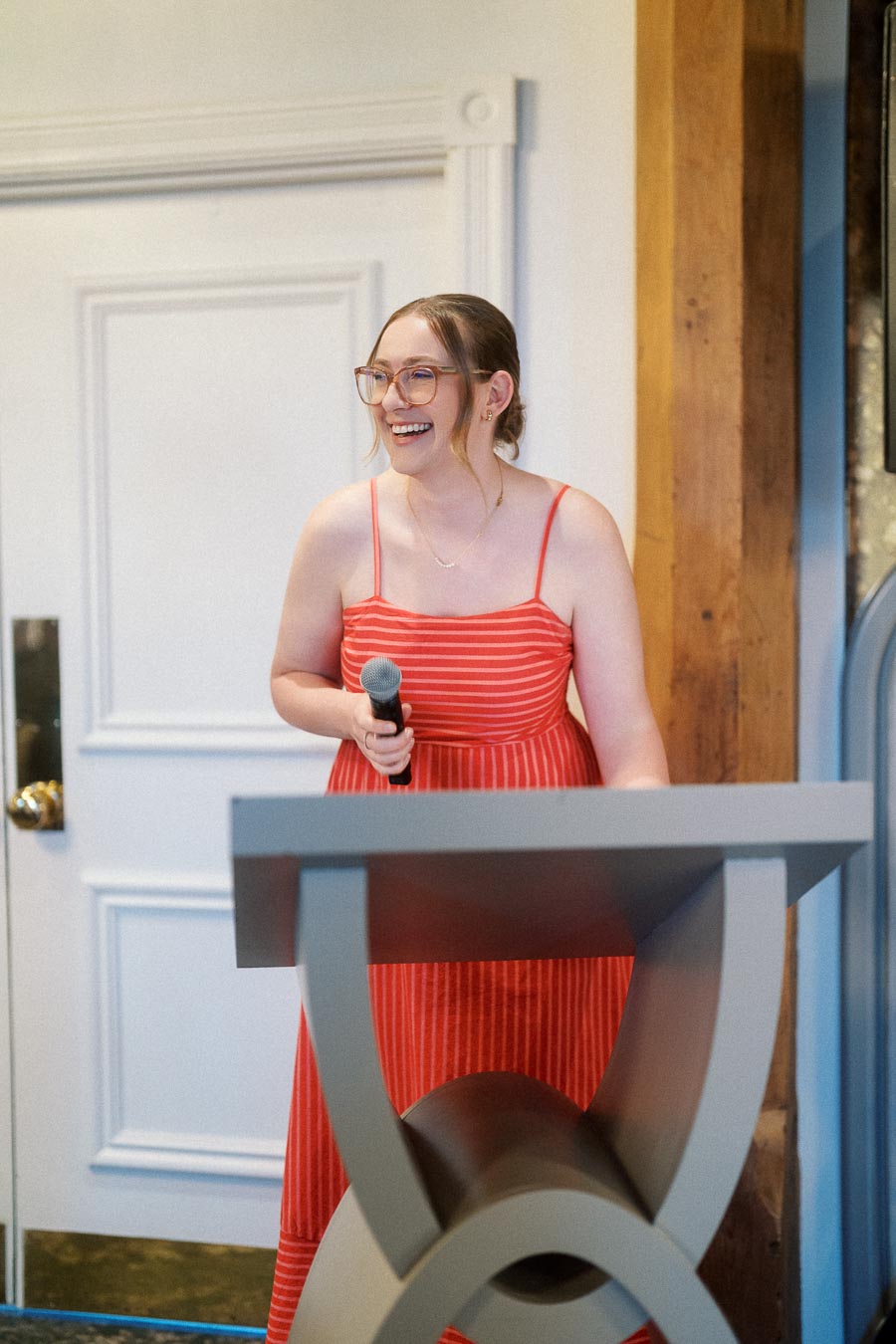 Woman in a red striped dress laughing while holding a microphone at a podium