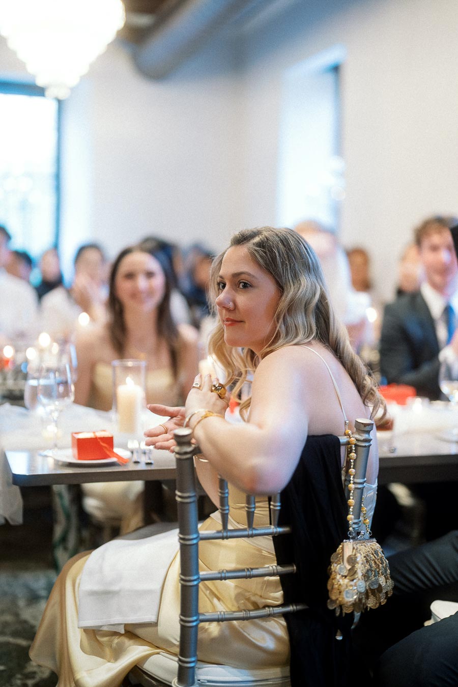 Woman in a formal dress seated at a candlelit reception table with guests behind her