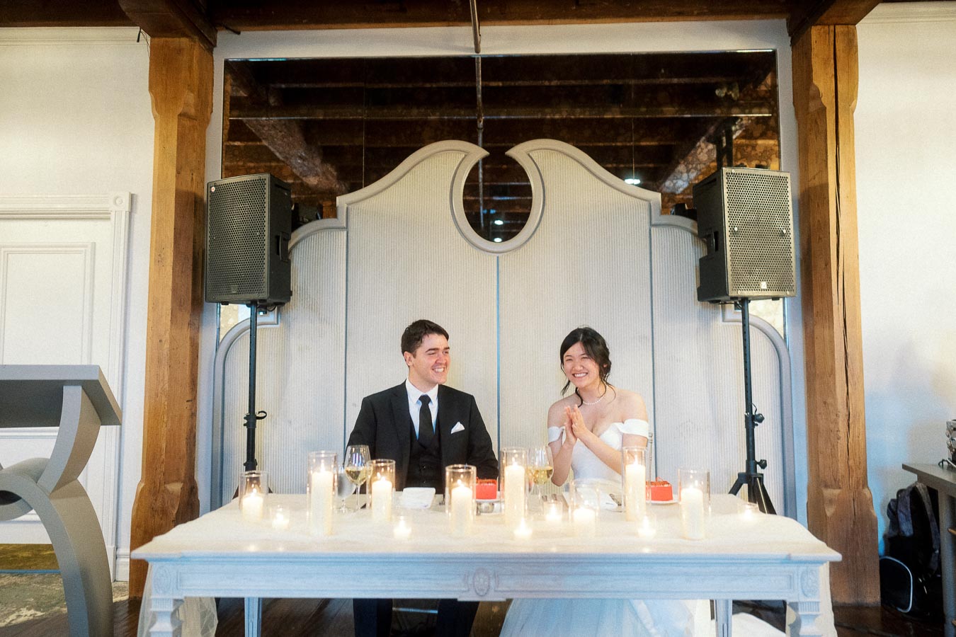 Couple seated at a candlelit table, smiling during a formal indoor celebration.