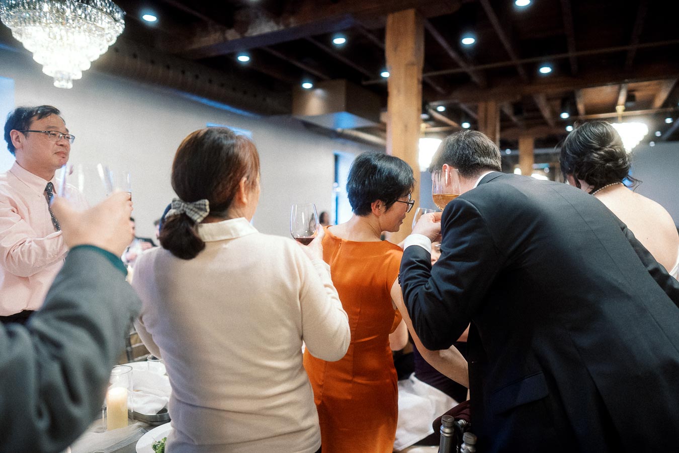 Wedding guests raise wine glasses during an indoor reception toast.