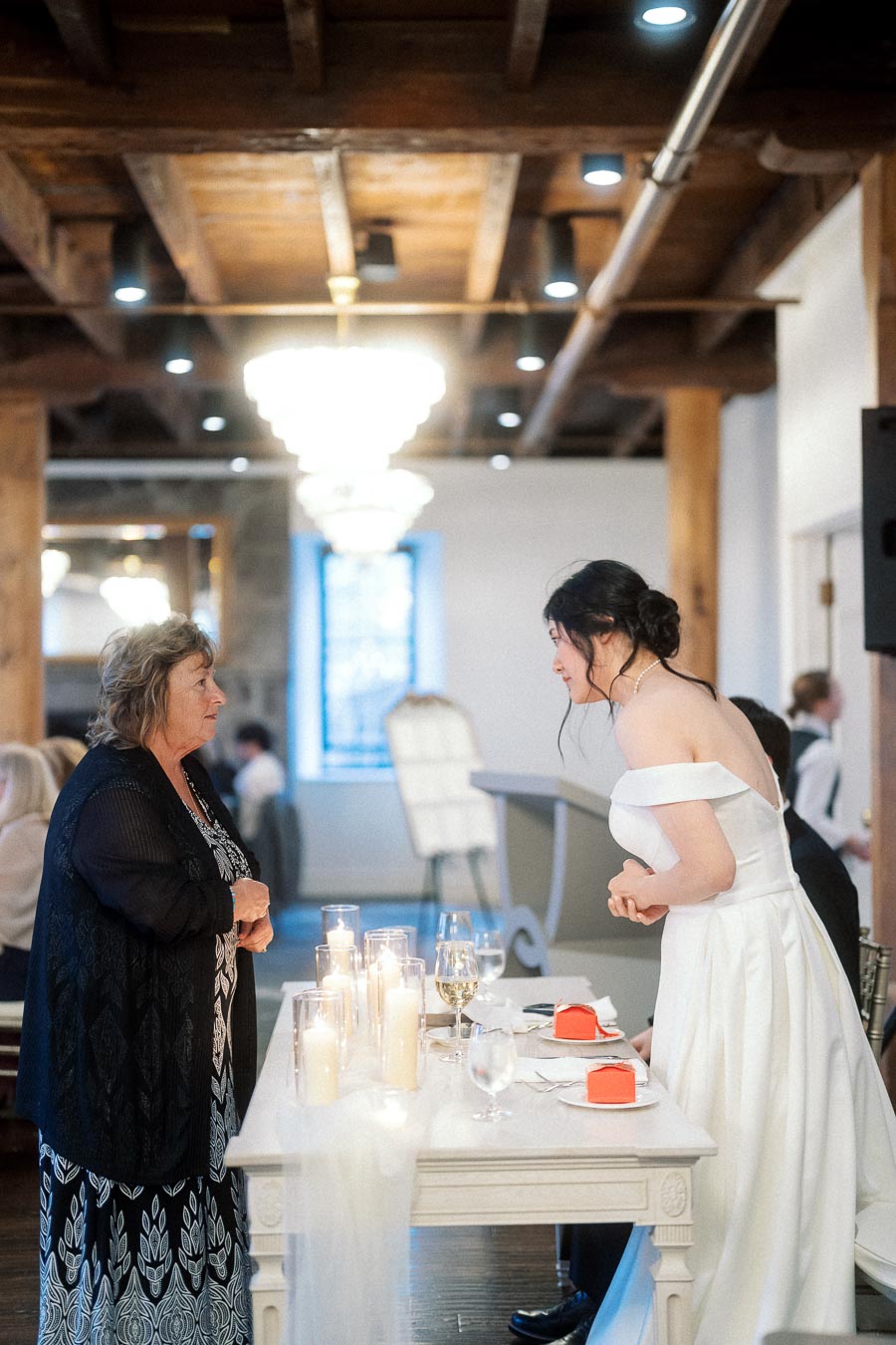 Woman in a white gown speaking with an older guest beside a candlelit table