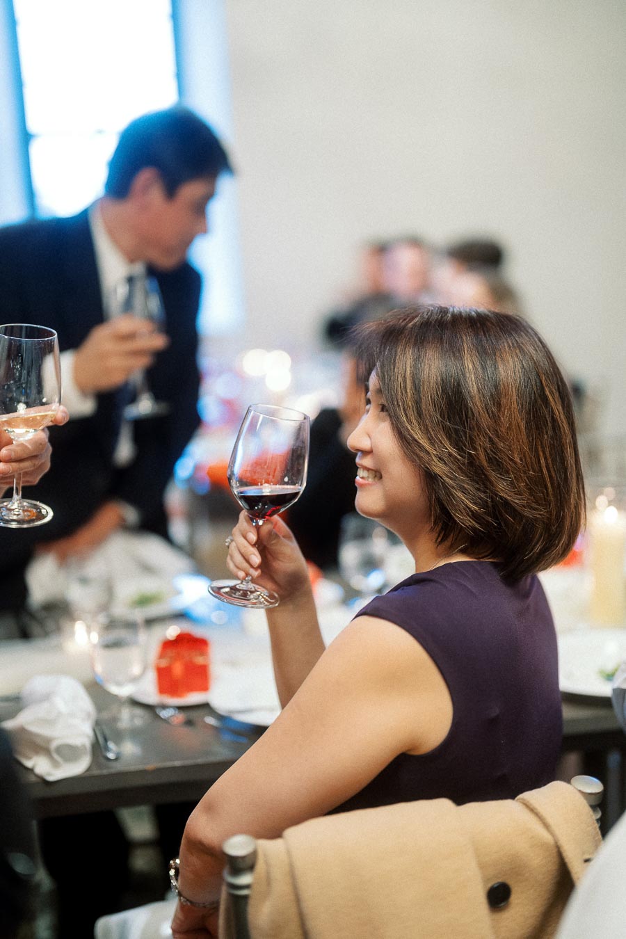 Woman smiling while holding a glass of red wine at a dinner table