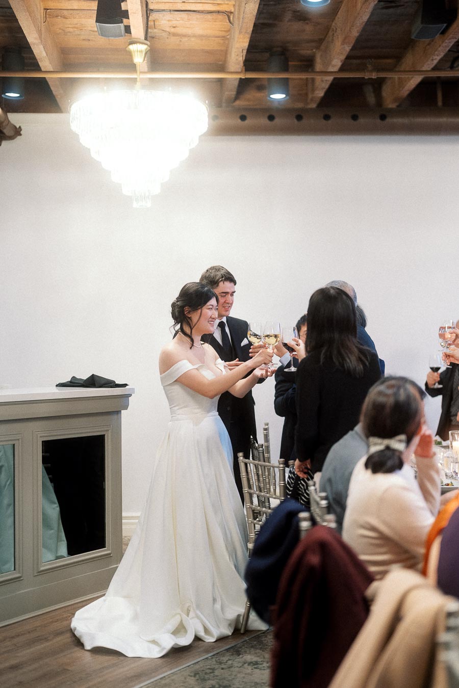 Couple in wedding attire toasting with guests during an indoor reception