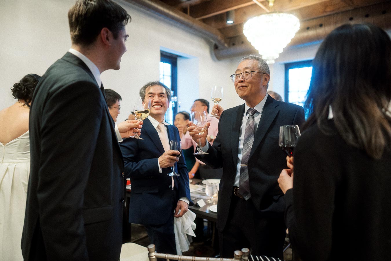 Guests in formal attire raise wine glasses during an indoor wedding reception toast.