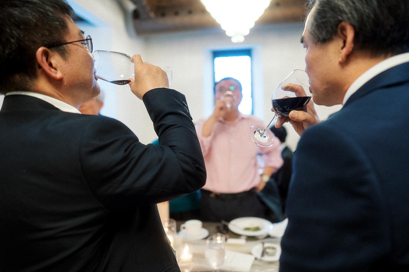 Guests in suits sip red wine during an indoor celebration dinner.
