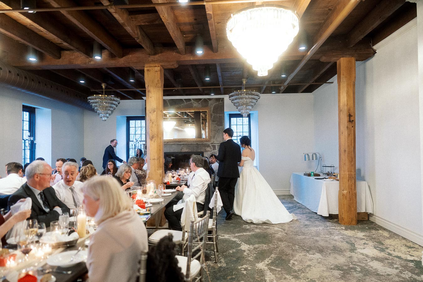 Bride and groom enter a reception room with seated dinner guests and chandeliers.