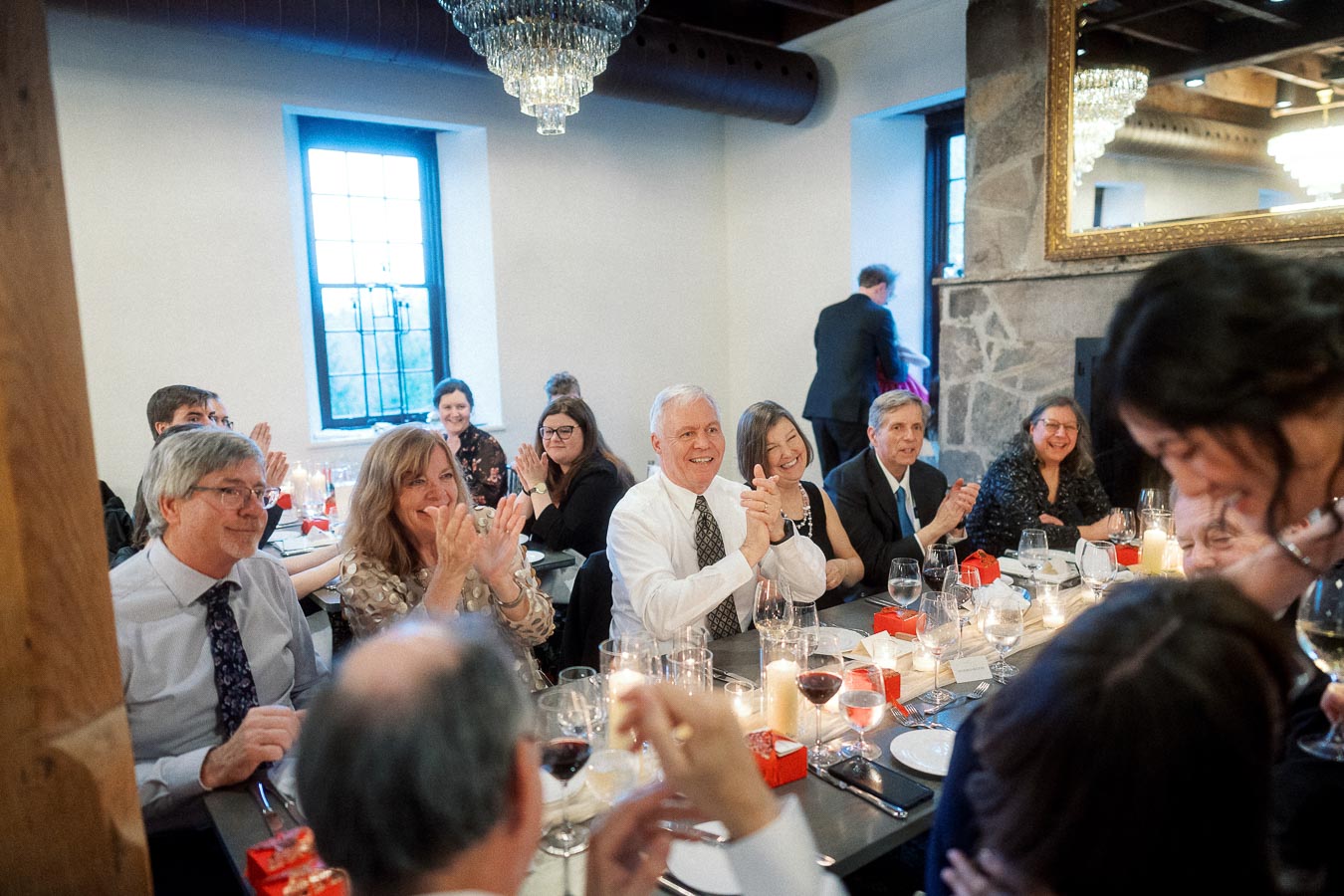 Guests seated at a dinner table applauding during an indoor celebration