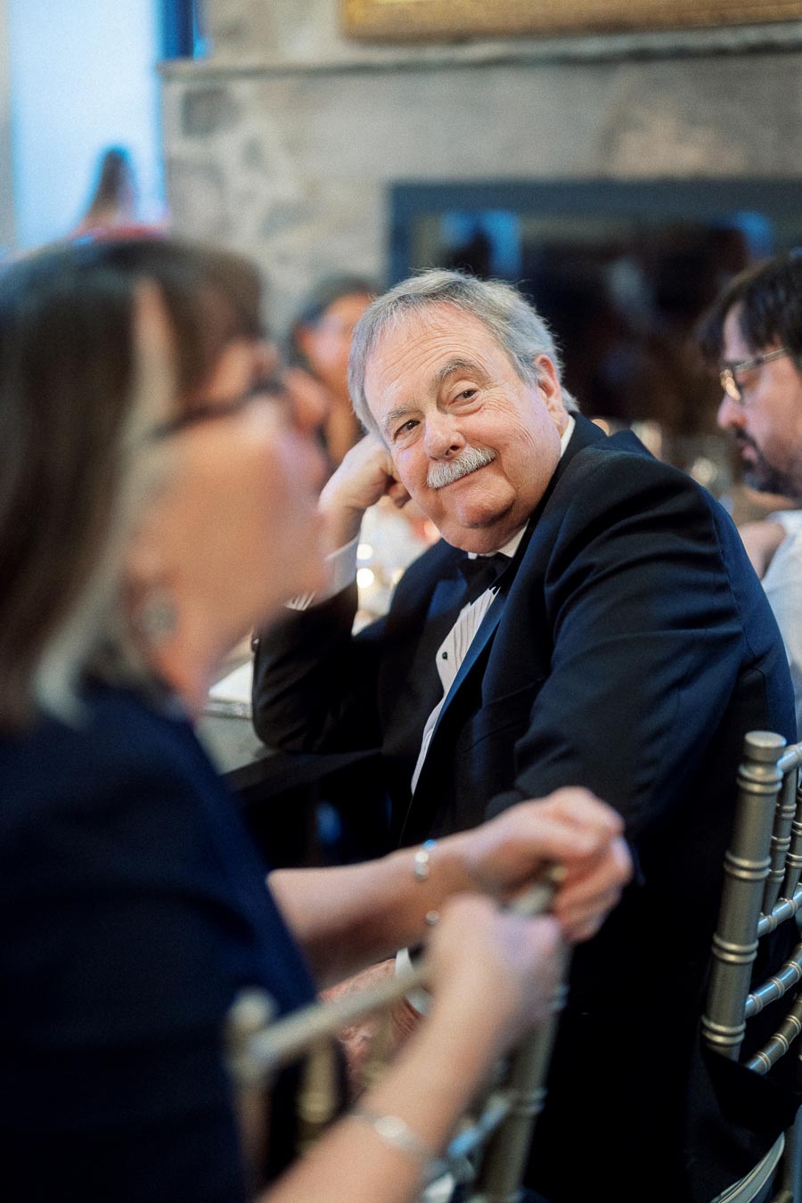 Man in a tuxedo smiling at a formal indoor table gathering