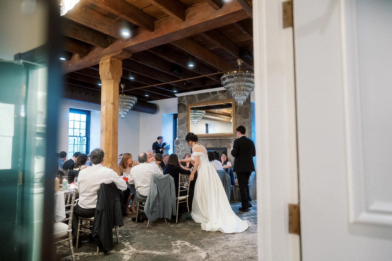 Bride and groom greet seated guests during an indoor reception dinner.