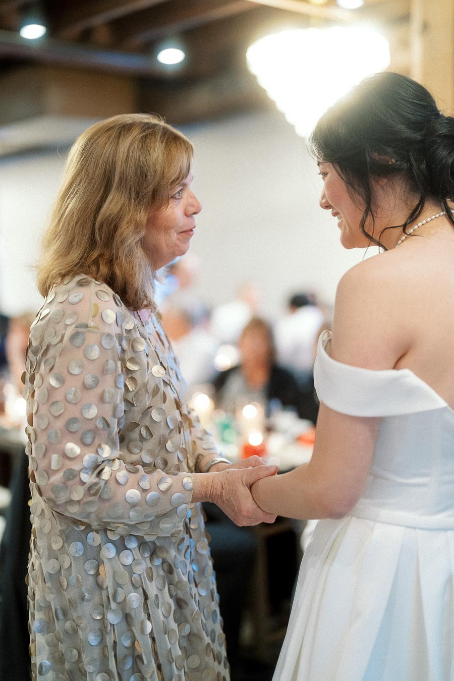 Woman in a white dress holding hands with an older woman at an indoor celebration