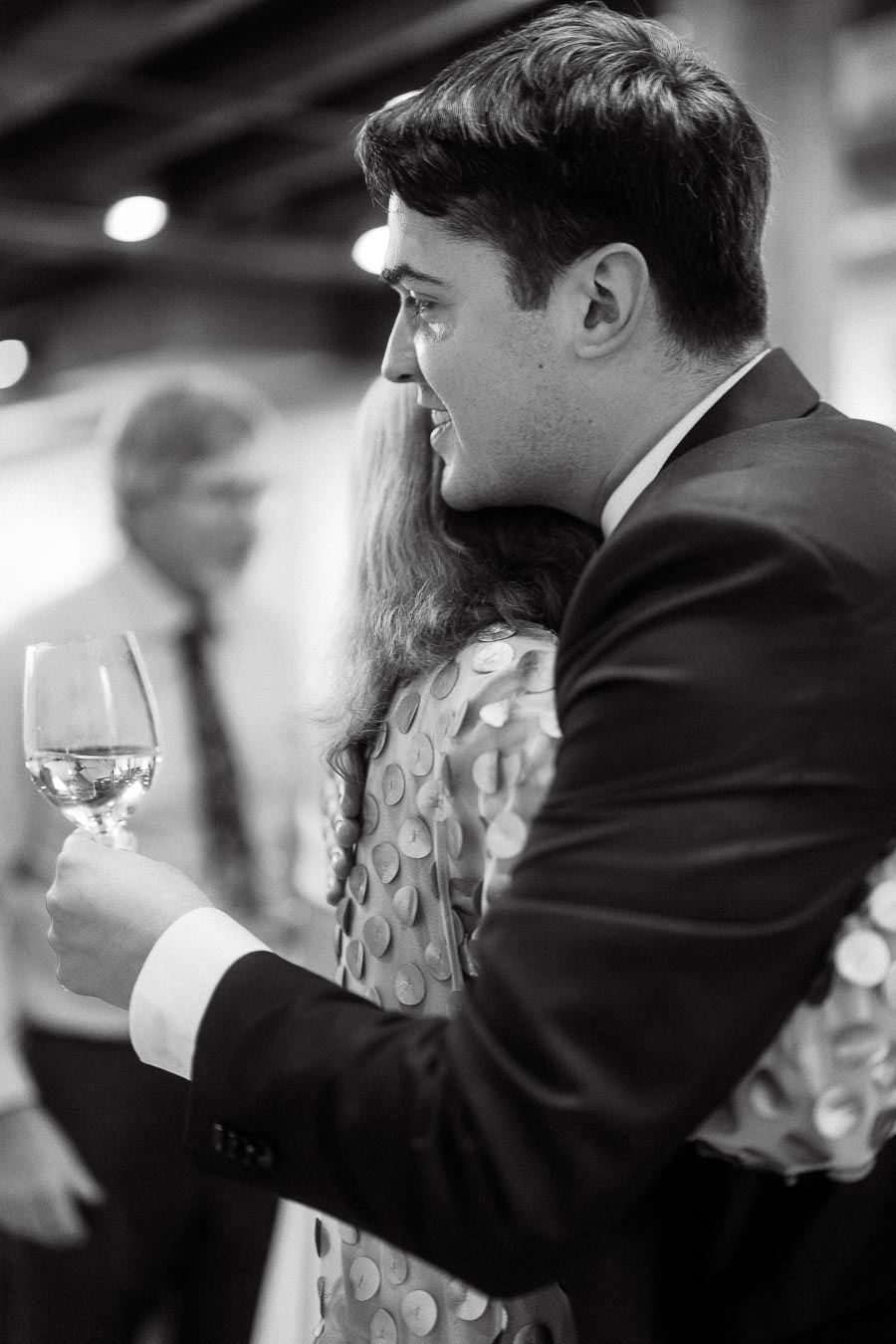 Couple embracing at an indoor event while one holds a wine glass