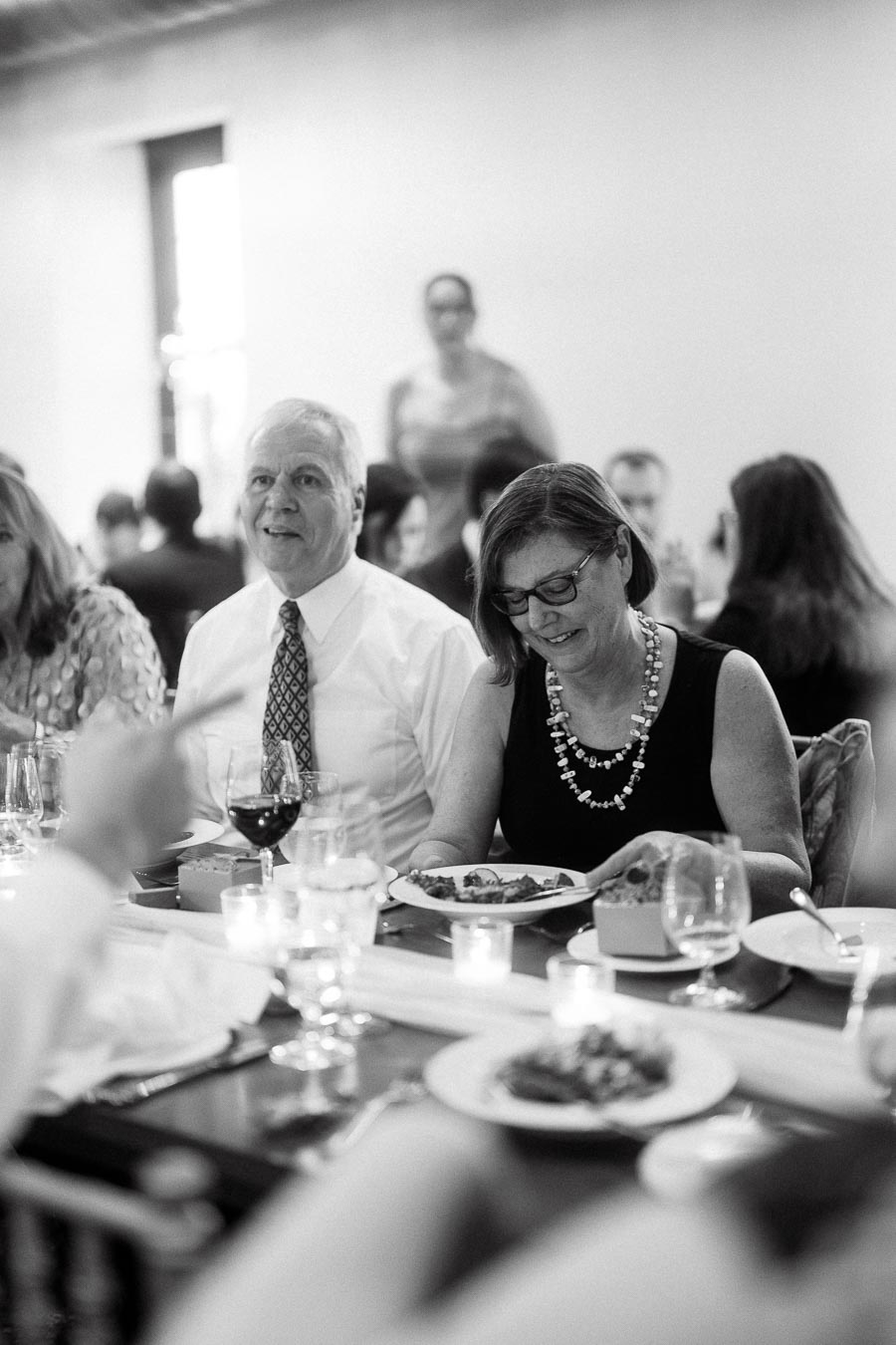 Guests seated at a formal dinner table with plates, wine glasses, and candles