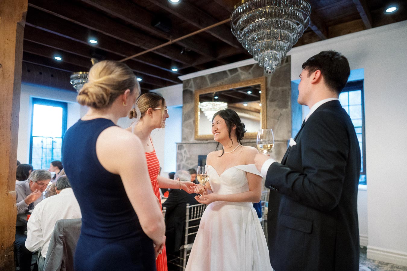 Bride and groom chat with guests holding wine glasses at an indoor reception.