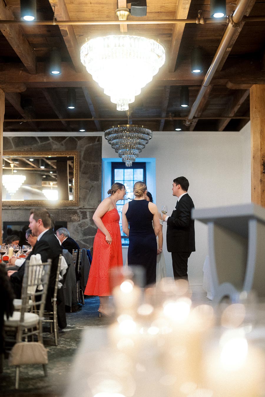 Guests in formal attire talking beneath chandeliers at an indoor reception