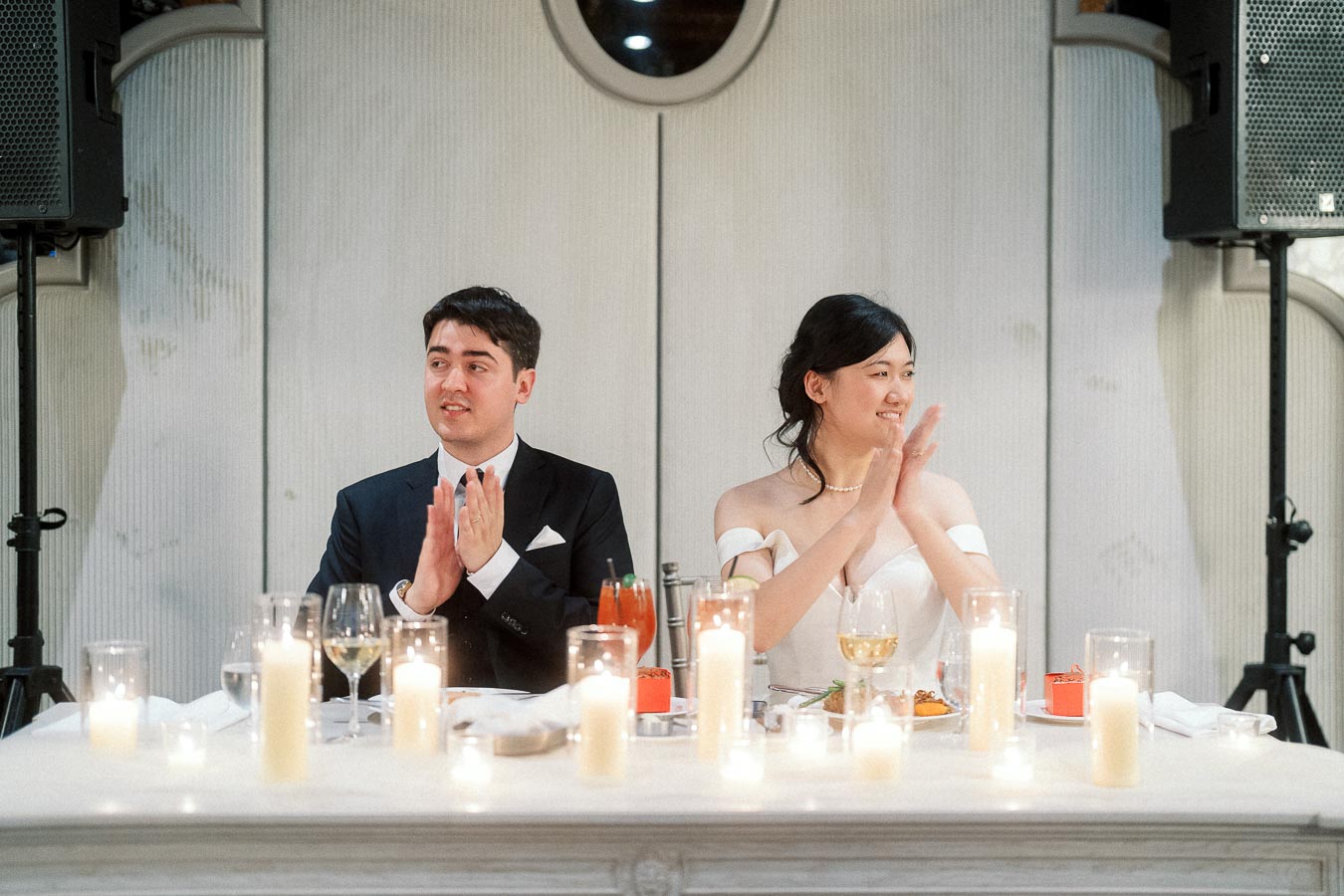 Couple in formal attire applauding at a candlelit reception table