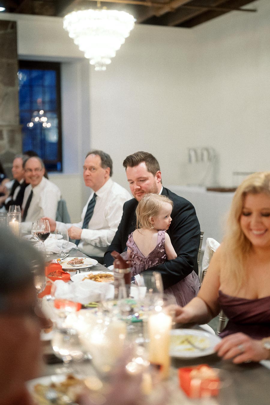 Man in a suit holding a young child at a candlelit dinner table