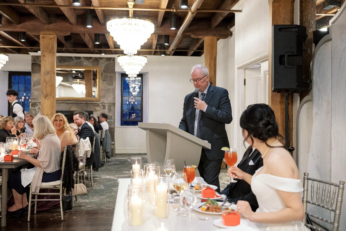 Man giving a speech at a formal reception while guests listen at dinner tables