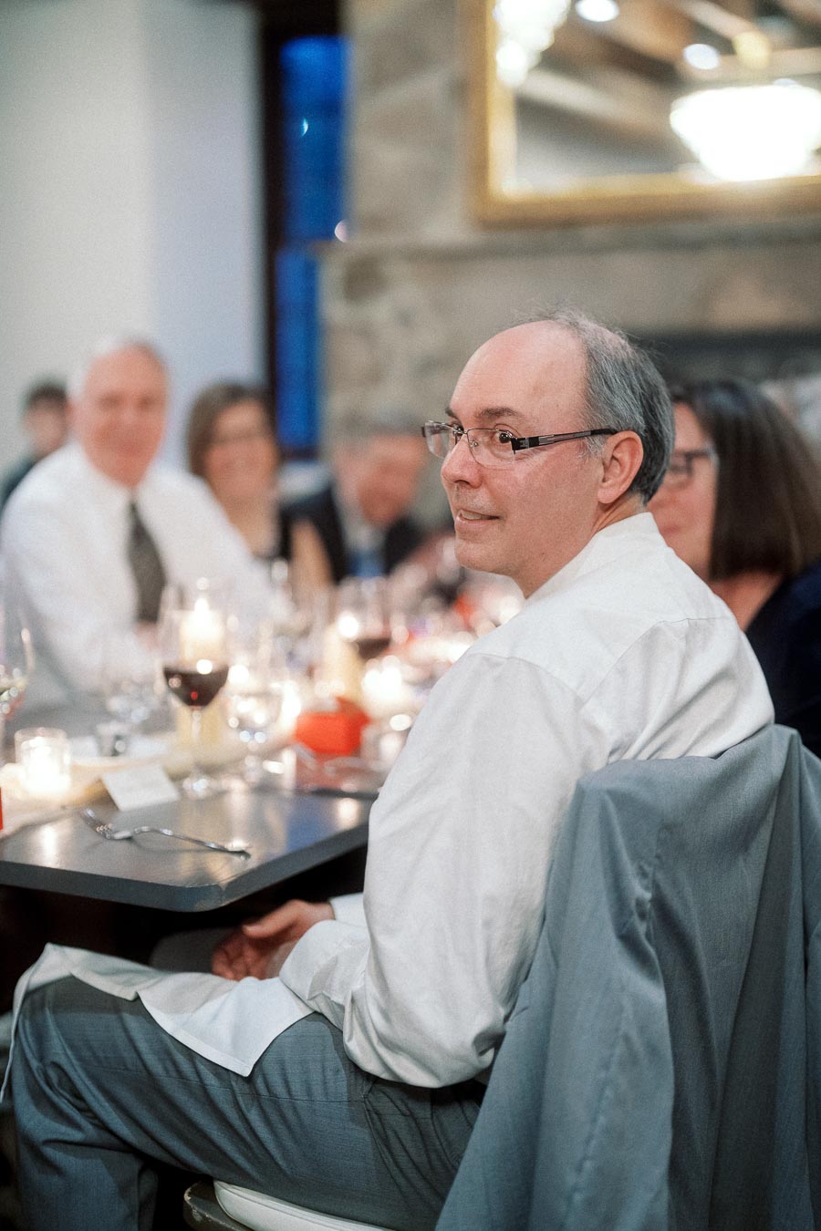 Man seated at a candlelit dinner table with guests in the background