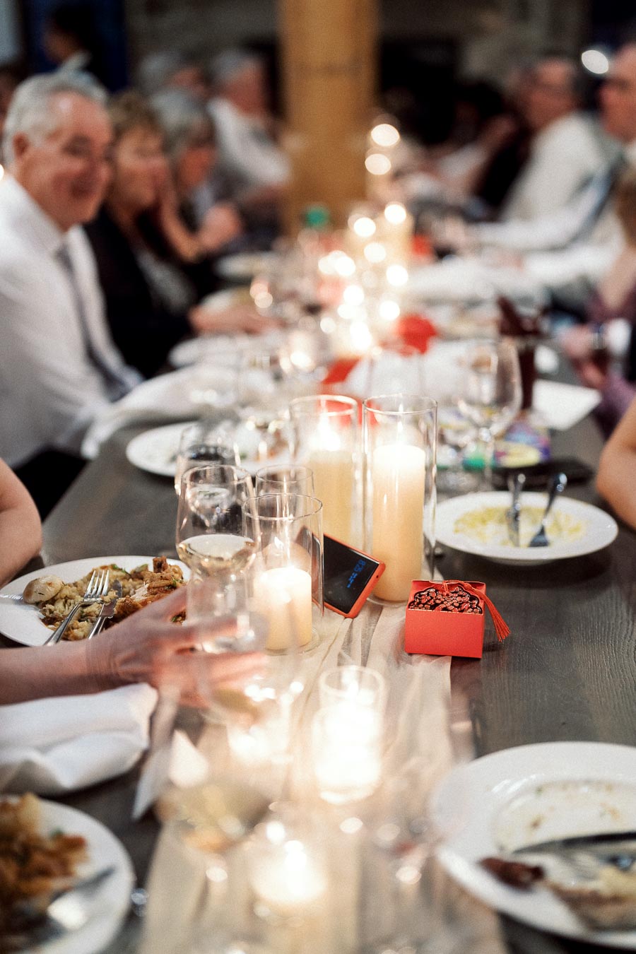 Candlelit dinner table with guests, wine glasses, plates, and a small red favor box.