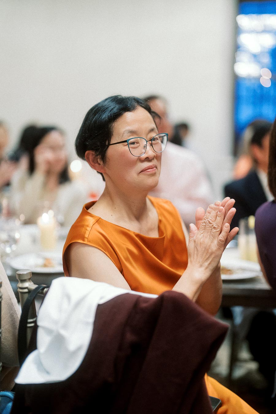 Woman in an orange dress applauding during an indoor celebration