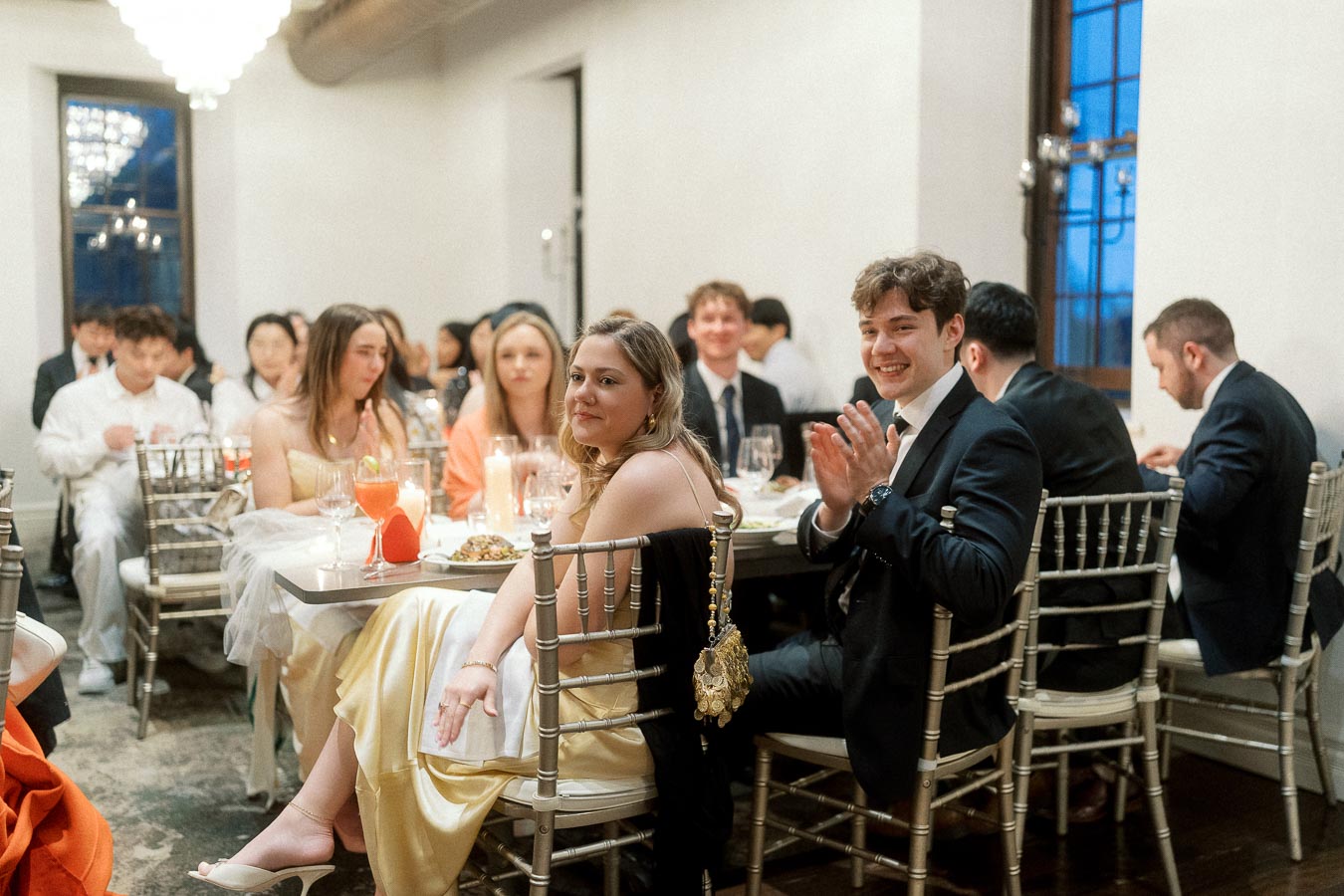 Guests seated at a formal dinner table, with one man smiling and applauding.