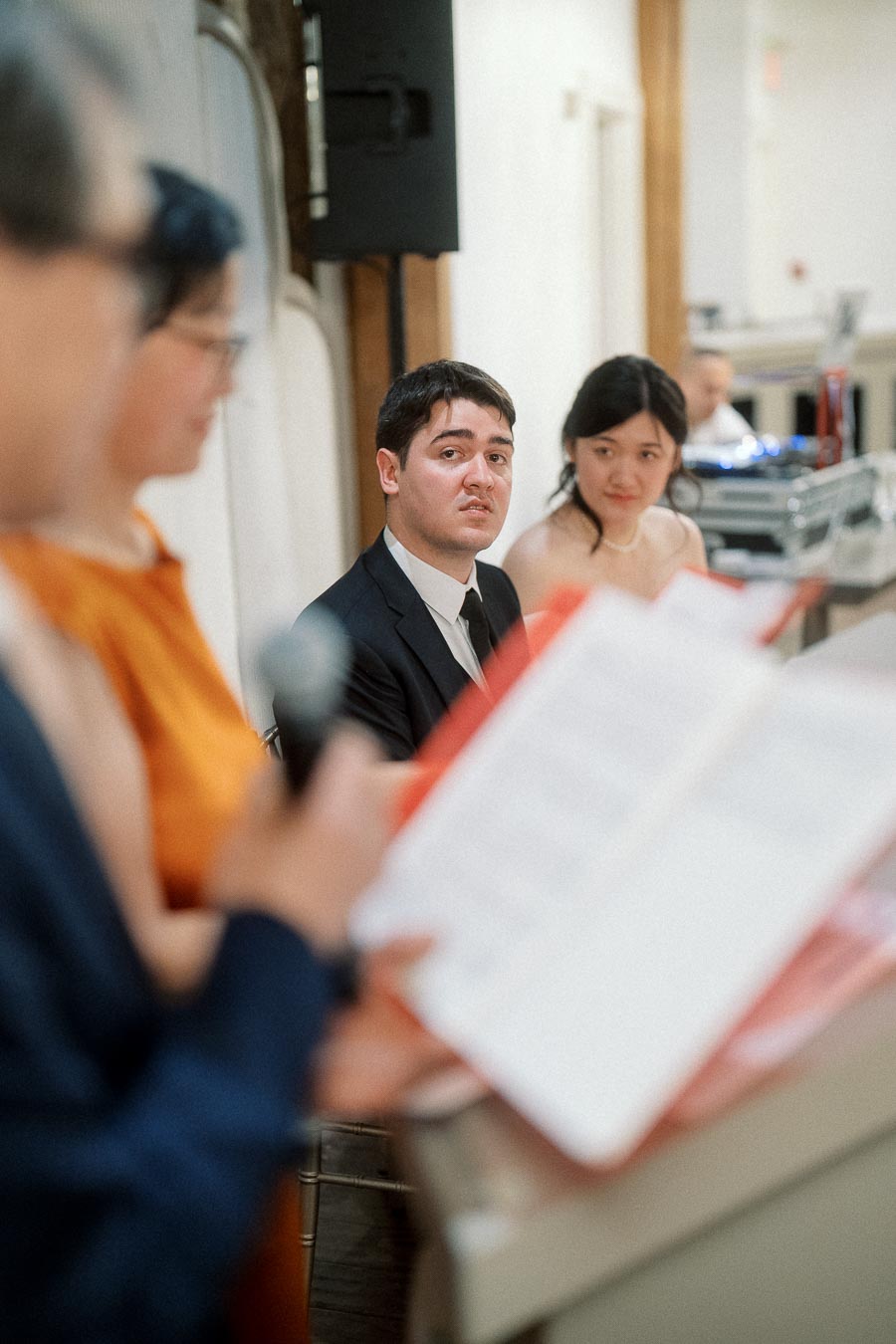 Couple seated indoors listening as a guest speaks into a microphone