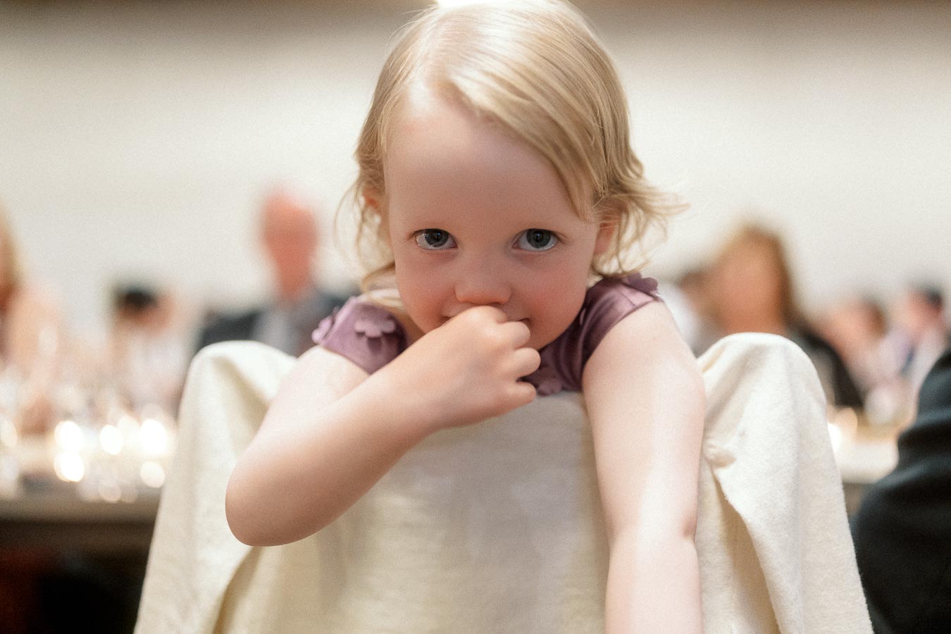 Young child leaning over a chair at a softly blurred indoor event