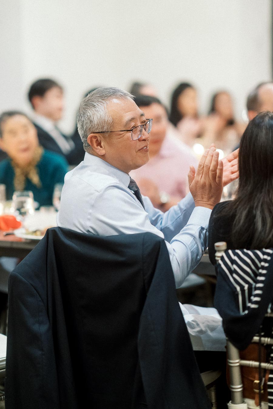 Man in glasses applauding while seated among guests at a formal indoor event