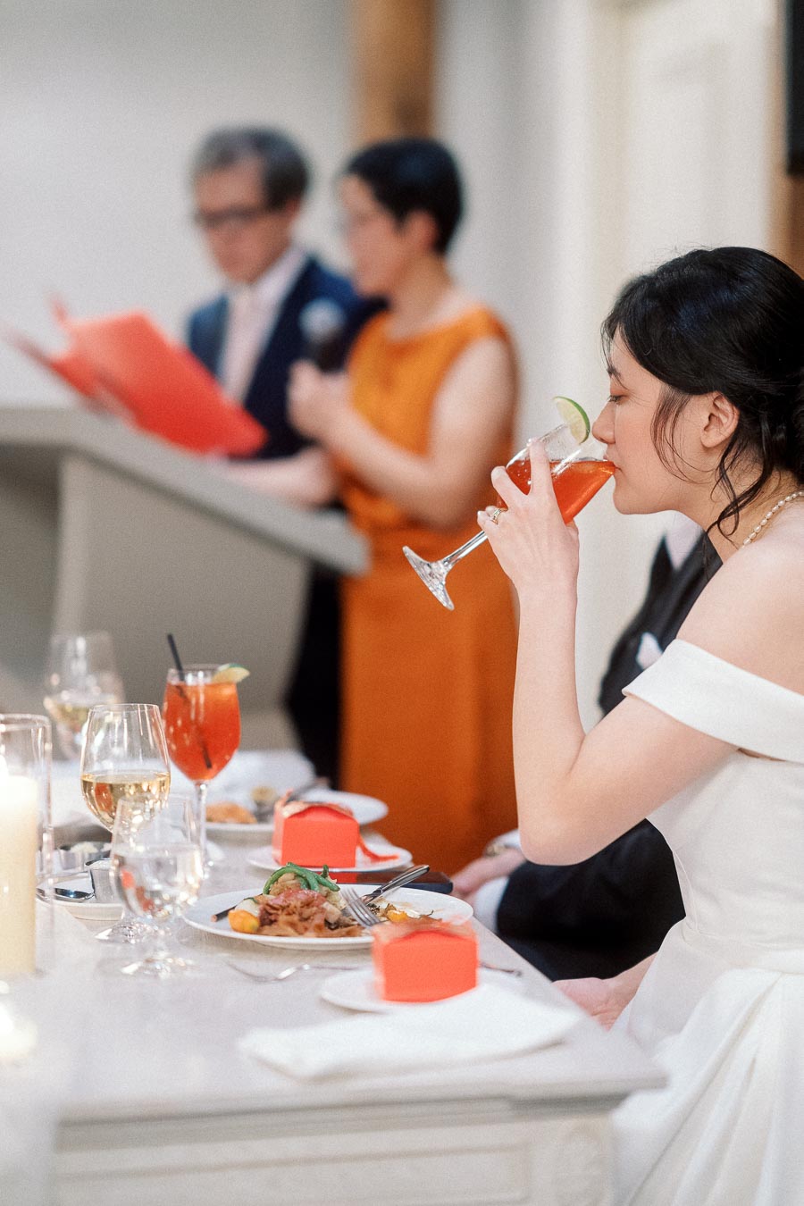 Woman in a white dress sipping a cocktail during a formal reception toast
