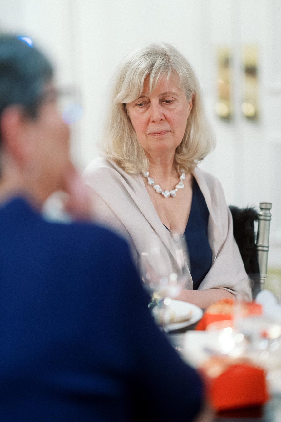 Woman seated at a formal table listening to a blurred guest nearby
