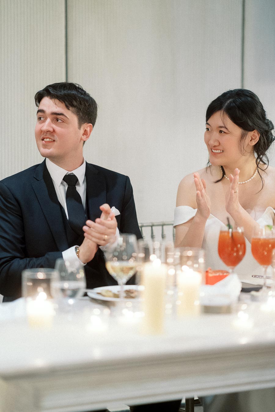 Couple in formal attire clapping at a candlelit table with drinks