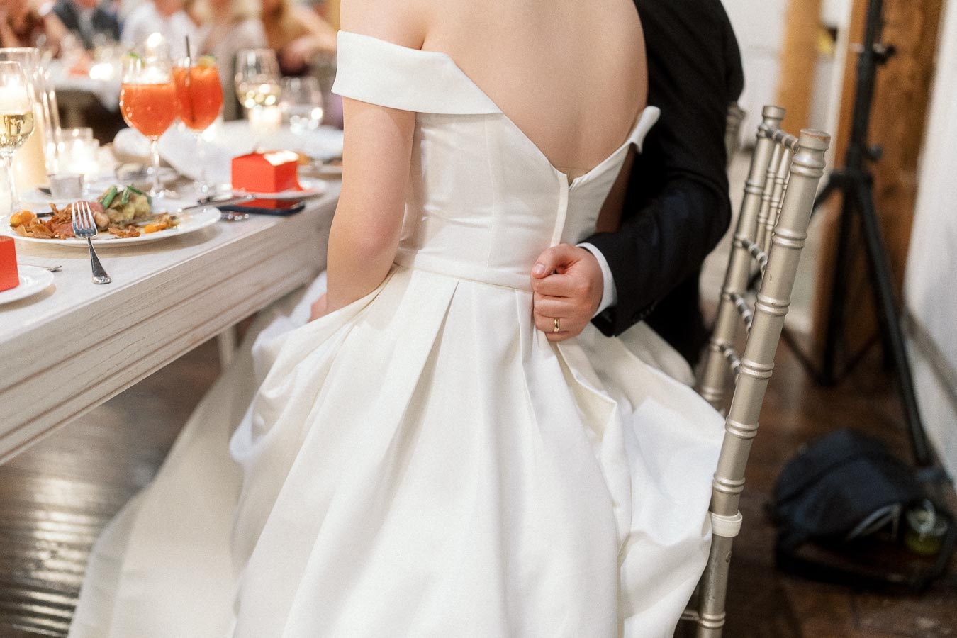Couple seated at a reception table, with a groom’s arm around a bride in a white gown