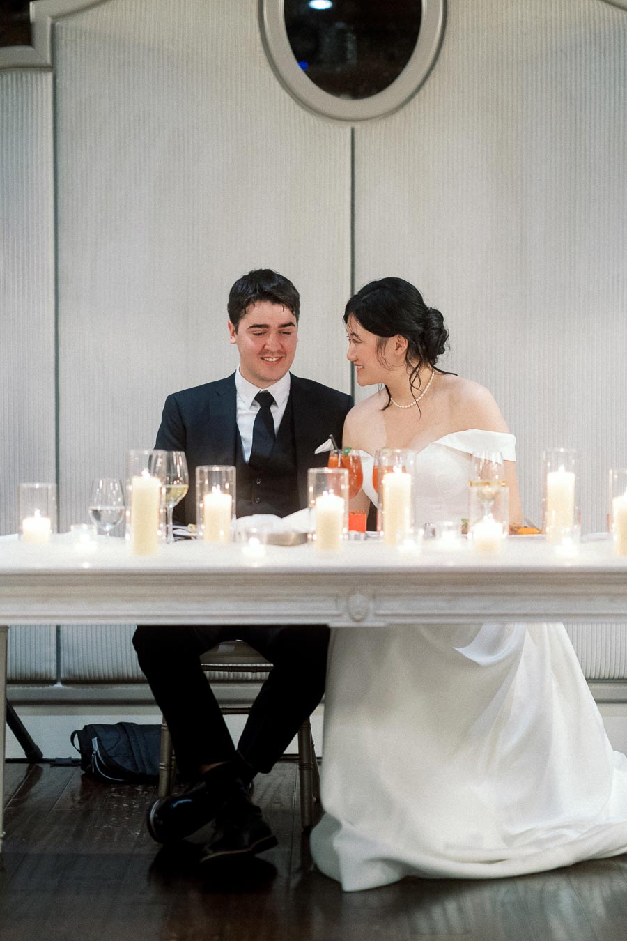 Couple in formal wedding attire seated together at a candlelit reception table