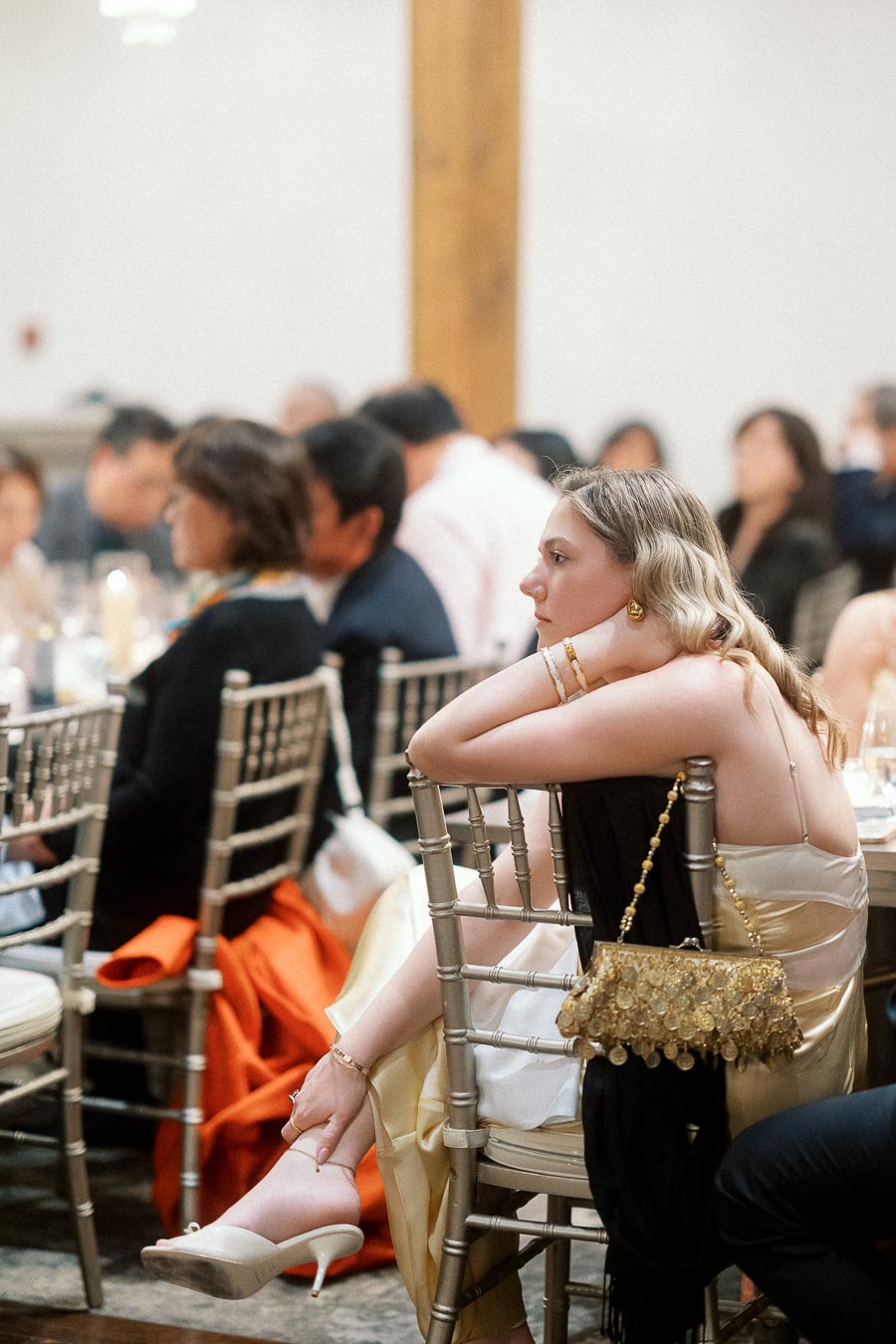 Woman in a satin dress seated among guests at a formal indoor event